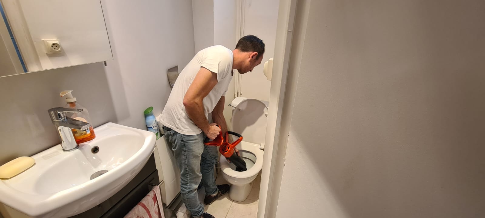 Homme réparant une toilette avec un débouchoir.